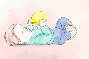 Baby liegt auf dem Rücken und hält in beiden Händen einen gelben Eimer